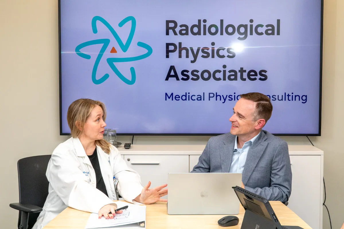 RadiologicalPhysicsAssociates-3586 RPA team members meeting in front of a screen showing the new Radiological Physics Associates logo