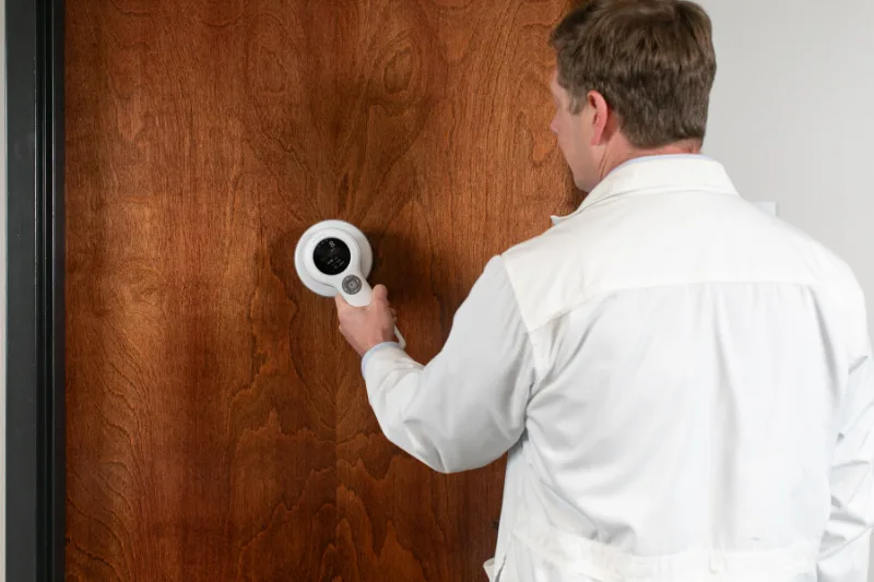 RadiologicalPhysicsAssociates-3102 Physicist in a lab coat holding a radiation survey meter against a door to check shielding